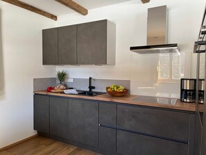 A modern kitchen with dark cabinets, a wooden countertop, a stainless steel range hood, and a coffee maker. - Sunnseitn, Germany (Bayrischzell)