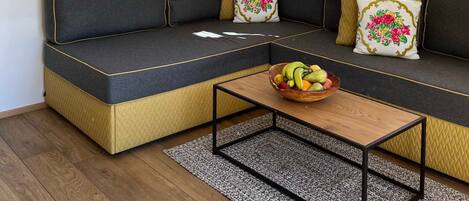 Una sala de estar moderna con un sofá modular, una mesa de centro de madera, un cuadro enmarcado de un paisaje y una ventana con cortinas.