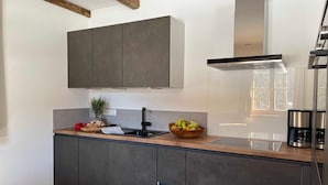 Une cuisine moderne avec des meubles de couleur sombre, un plan de travail en bois, une hotte de cuisine en acier inoxydable et une machine à café.