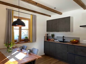 A modern kitchen with a dining area, featuring a wooden table, chairs, a pendant light, and a view of the outdoors.