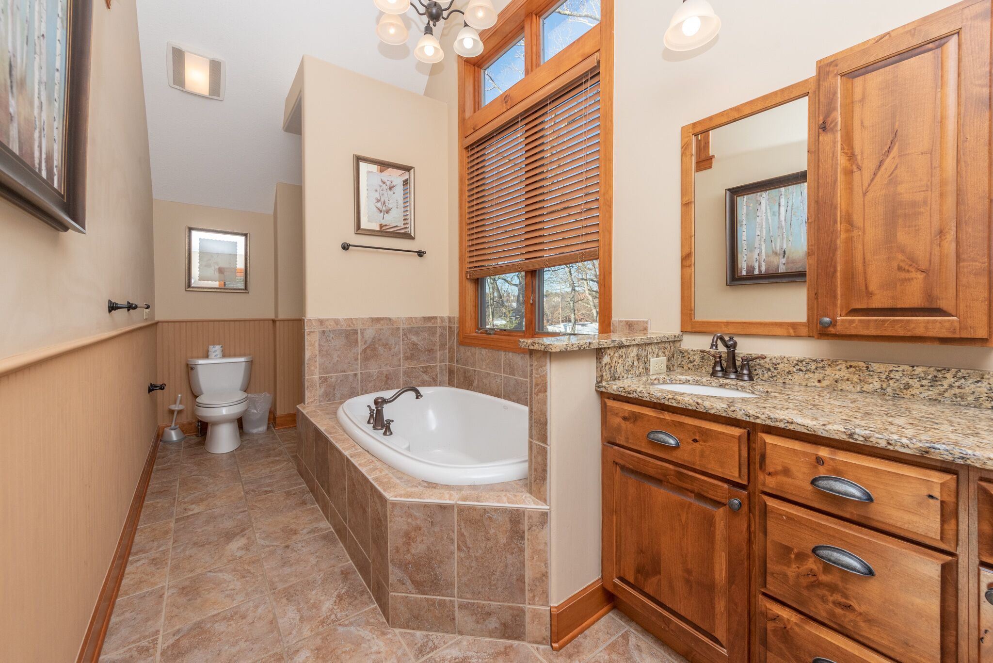 A bathroom with a bathtub, sink, wooden cabinets, and a window with blinds.
