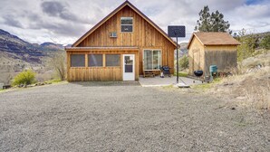 A wooden cabin with a large garage, a small shed, and a gravel driveway.