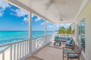 A covered outdoor area with a view of the ocean, a pool, and a seating area with cushions. - Beach Front Villa LAS with direct Beach access (Nassau)