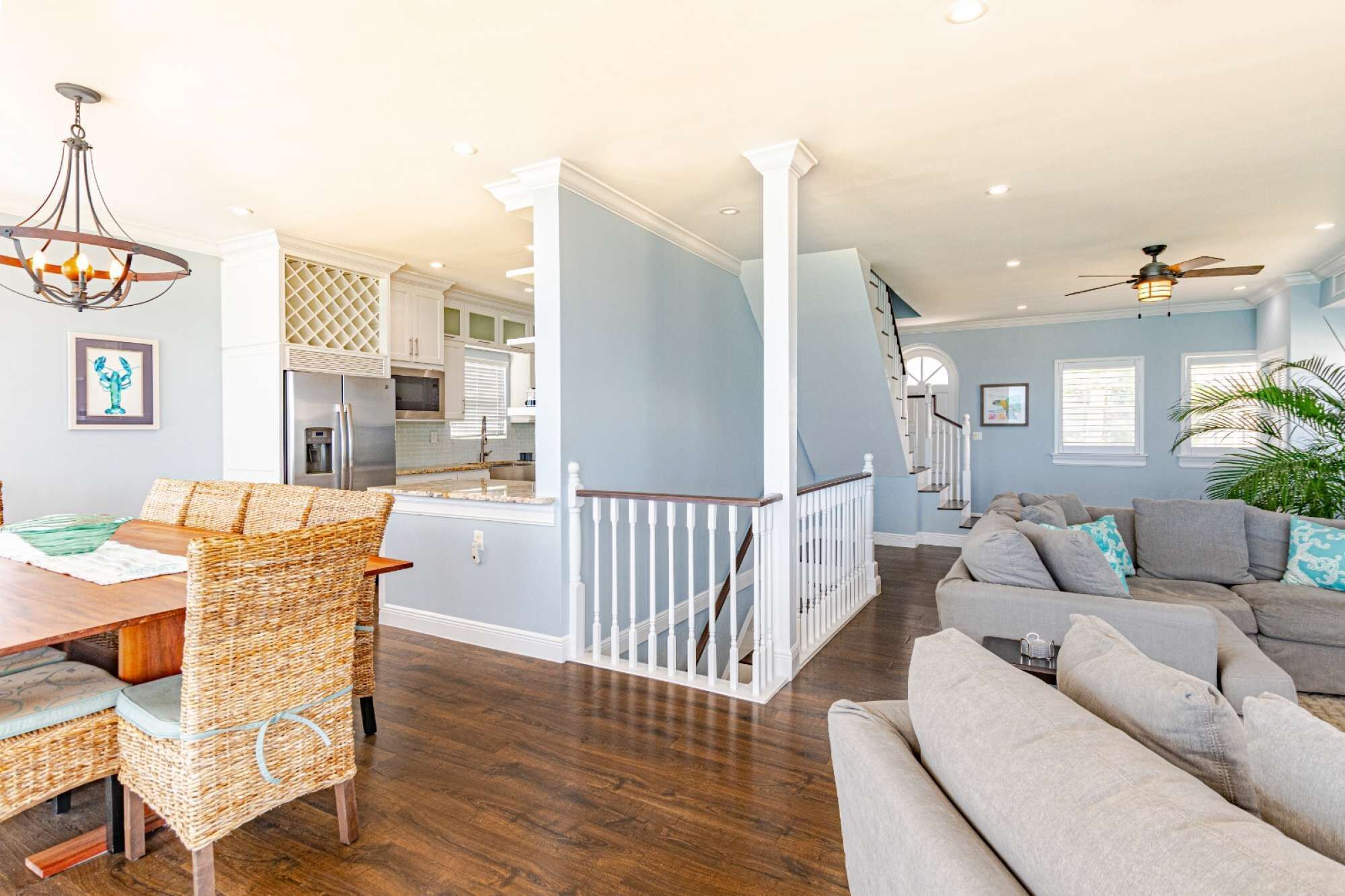 A spacious living area with a dining table and wicker chairs, a staircase leading to an upper level, and a modern kitchen in the background.