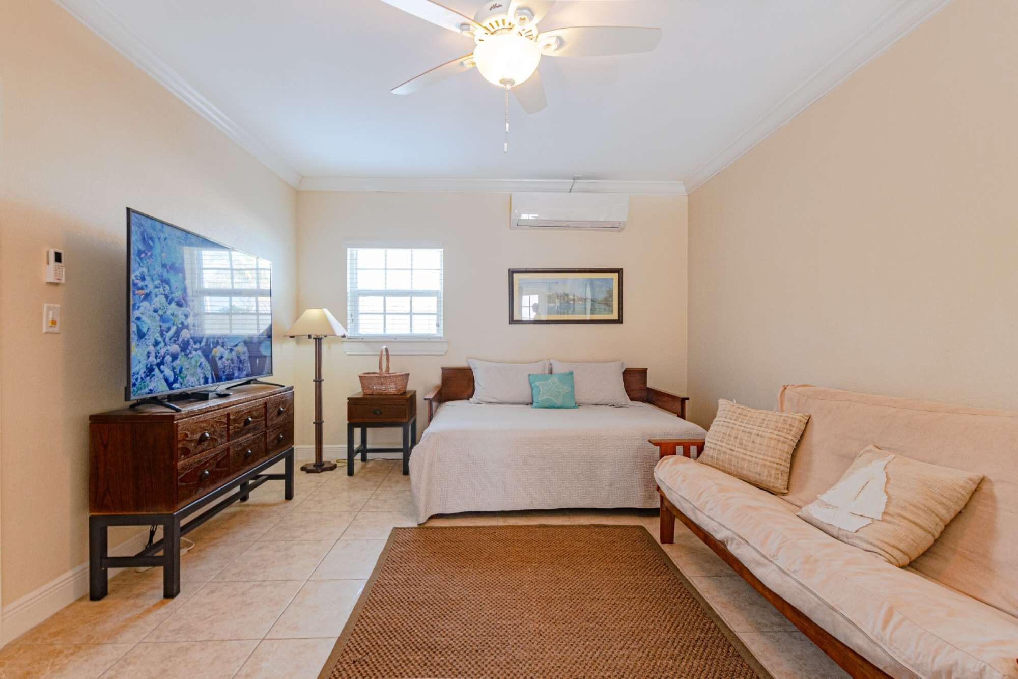 A bedroom with a bed, a sofa, a TV, a ceiling fan, and a window.