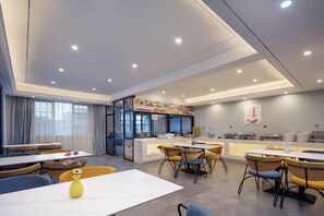 A modern dining area with tables and chairs, a kitchen counter, and a view of the city. - Tingxi International Hotel (Changsha County)