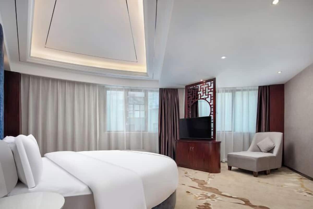 A hotel room with a bed, a TV, a chair, and a decorative wall piece.
