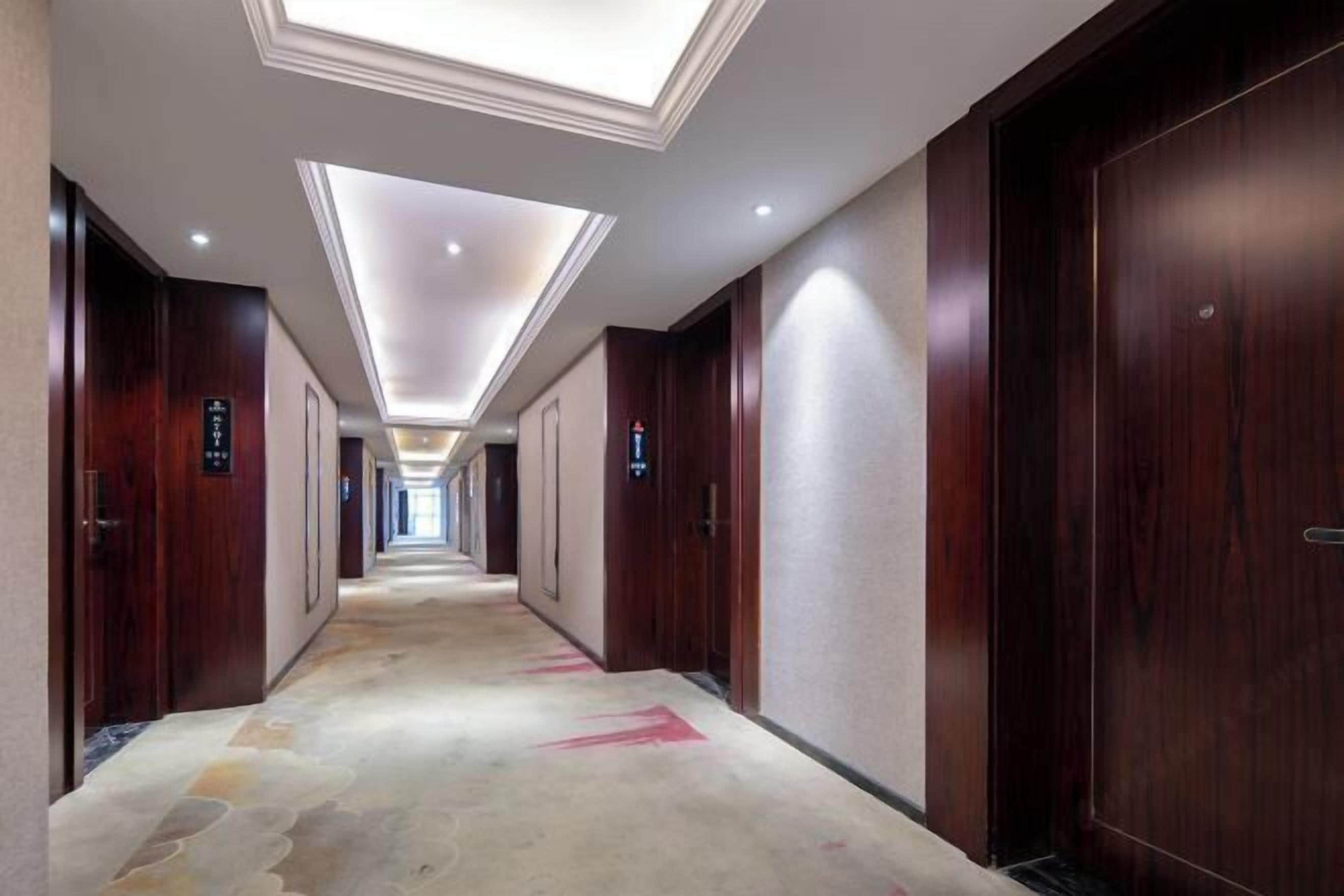 A hotel corridor with wooden doors, a patterned carpet, and a skylight ceiling.