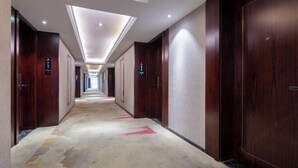 A hotel corridor with wooden doors, a patterned carpet, and a skylight ceiling. - Tingxi International Hotel (Changsha County)