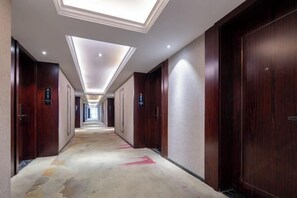 A hotel corridor with wooden doors, a patterned carpet, and a skylight ceiling. - Tingxi International Hotel (Changsha County)