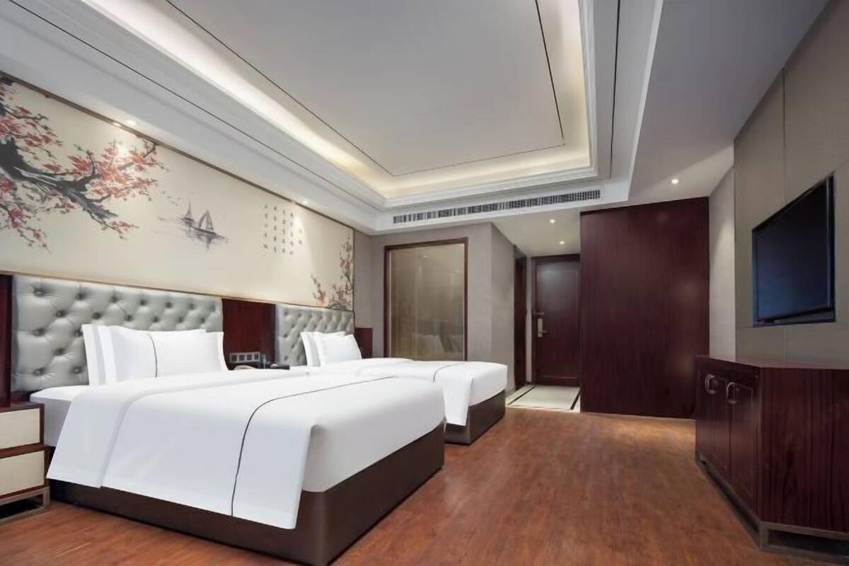 A hotel room with a large bed, a smaller bed, a wardrobe, a television, and a decorative wall.