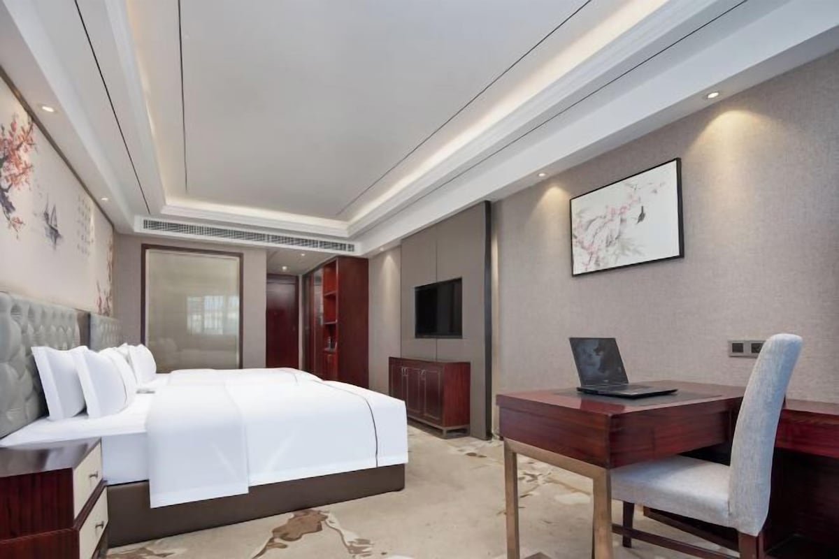 A hotel room with a bed, a desk with a laptop, a TV, and a large mirror.
