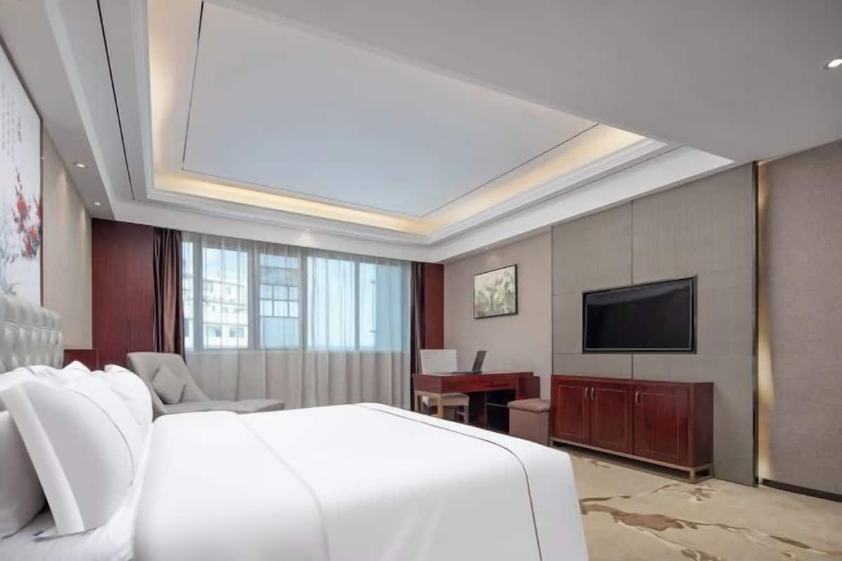 A hotel room with a bed, a desk, a chair, a television, and a large window.