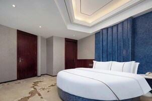 Habitación de hotel con una cama grande, dos puertas, una pared azul de acento e iluminación empotrada en el techo.