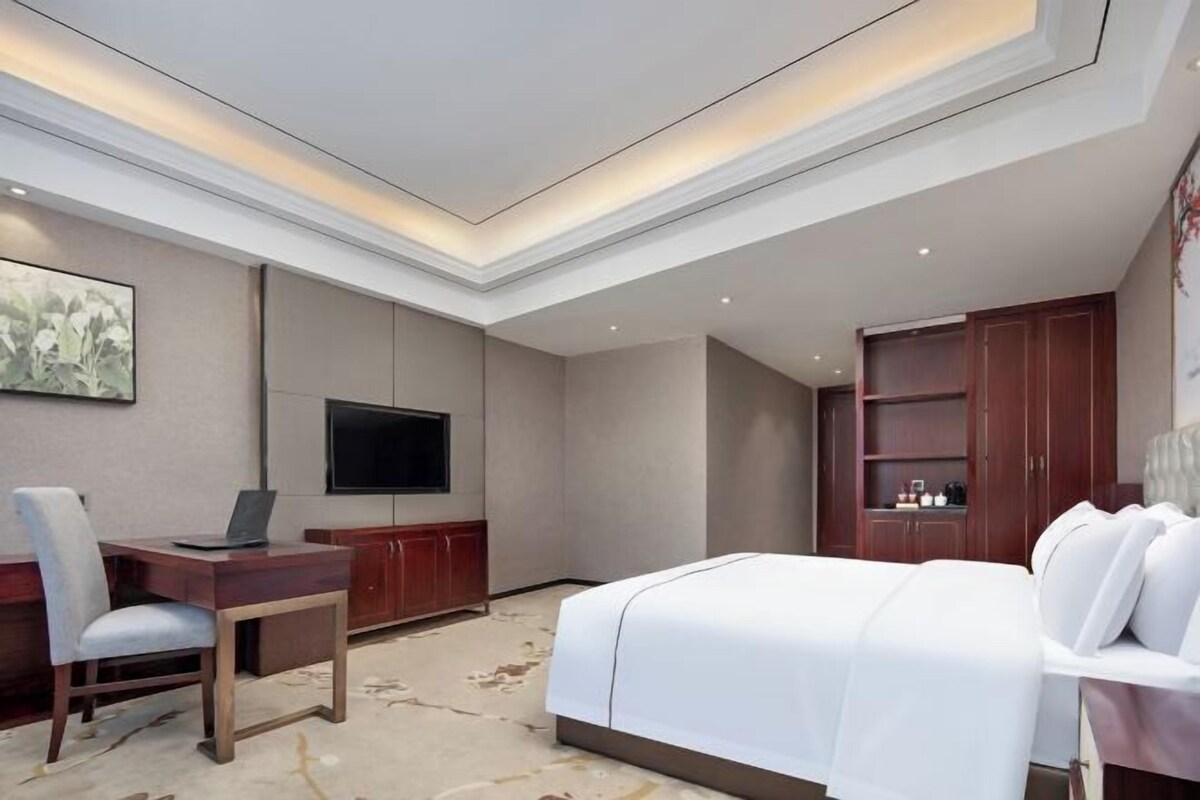 A hotel room with a bed, desk, chair, television, and a cabinet.
