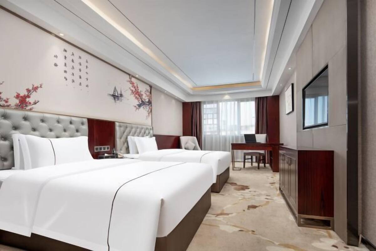 A hotel room with a large bed, a smaller bed, a desk, and a TV.