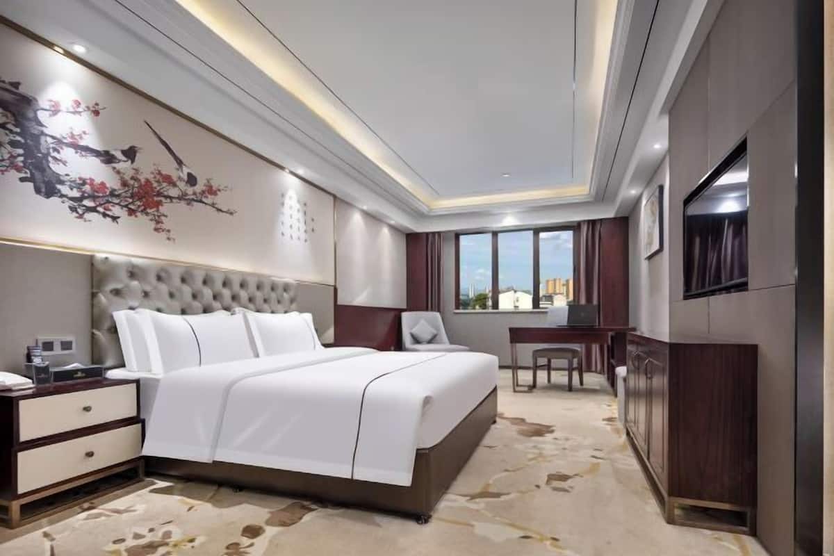 A modern hotel room with a large bed, a desk, and a view of the city.