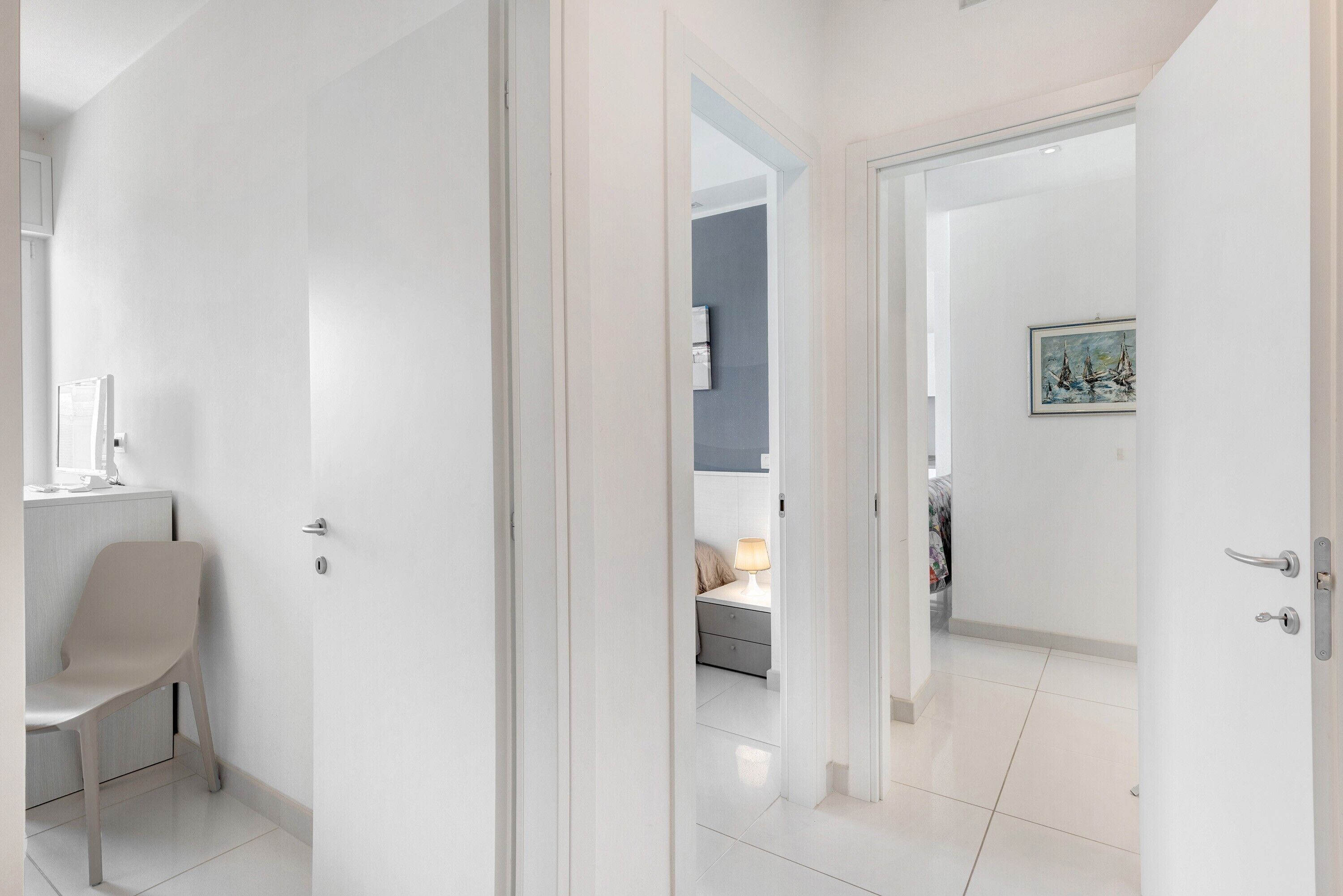A modern interior with a white door, a chair, a bed, and a painting on the wall.