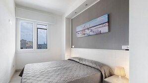 A bedroom with a bed, a nightstand, a lamp, a window, and a painting on the wall. - Apartment "Ca Laurana 42" with Sea View, Air Conditioning and Terrace (Bibione)