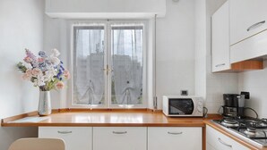 Una cucina con mobili bianchi, un forno a microonde, un fornello e una finestra con tende.