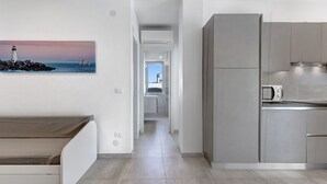 Ett modernt kök med inbyggda vitvaror, en matplats med en bänk och en hall som leder till ett sovrum.