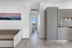 Una cocina moderna con electrodomésticos integrados, un comedor con banco y un pasillo que conduce a un dormitorio.