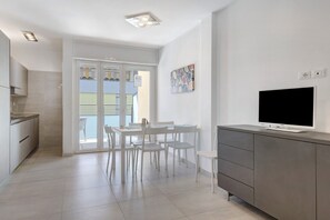 Una cocina moderna con comedor, un televisor en un mueble y un balcón con vistas.
