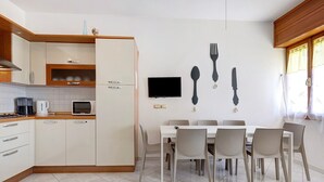 A modern kitchen with white cabinets, a dining table with chairs, a flat-screen TV, and wall-mounted cutlery. - Apartment 'Ca Laurana 52' near the beach with garden and terrace (Bibione)