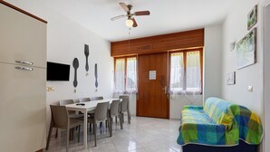 A dining area with a table and chairs, a television, and a ceiling fan. - Apartment 'Ca Laurana 52' near the beach with garden and terrace (Bibione)