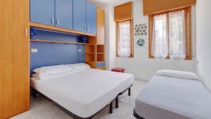 A bedroom with a bed, a smaller bed, a wardrobe, a shelf, and a window with curtains. - Apartment 'Ca Laurana 52' near the beach with garden and terrace (Bibione)