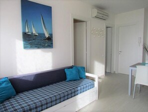 A modern room with a sofa, a painting of sailboats, an air conditioning unit, and a door. - Apartment 'Condominio Zenit' with Sea View and Garden (Bibione)