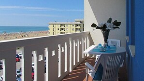 Een balkon met uitzicht op het strand, een tafel met een bloevas en een stoel.