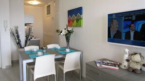 Een eetgedeelte met een tafel, stoelen, een vaas met bloemen, een televisiescherm en een teddybeer.