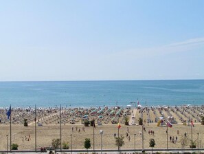 Una playa con hileras de sombrillas y tumbonas, un cielo despejado y el mar al fondo.