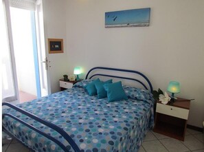 A bedroom with a bed, two bedside tables, a nightstand, a painting, and a door. - Apartment 'Condominio Zenit' with Sea View and Garden (Bibione)