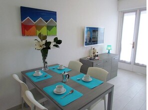 A dining area with a table set for four, a vase with flowers, a painting, and a framed picture on the wall. - Apartment 'Condominio Zenit' with Sea View and Garden (Bibione)