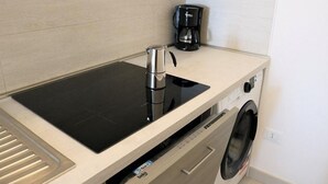 Een kitchenette met een zwart inductiekookplaatje, een koffiezetapparaat en een ingebouwde wasmachine.