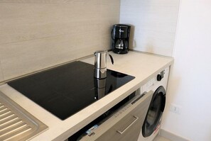 Uma cozinha compacta com um fogão por indução preto, cafeteira e máquina de lavar embutida.