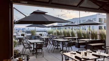 Un área de comedor al aire libre con mesas, sillas, sombrillas y plantas en macetas.