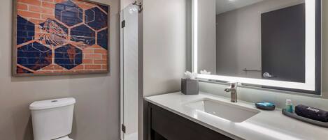 A modern bathroom with a white toilet, a glass shower enclosure, a large mirror, and a white sink with a dark vanity.