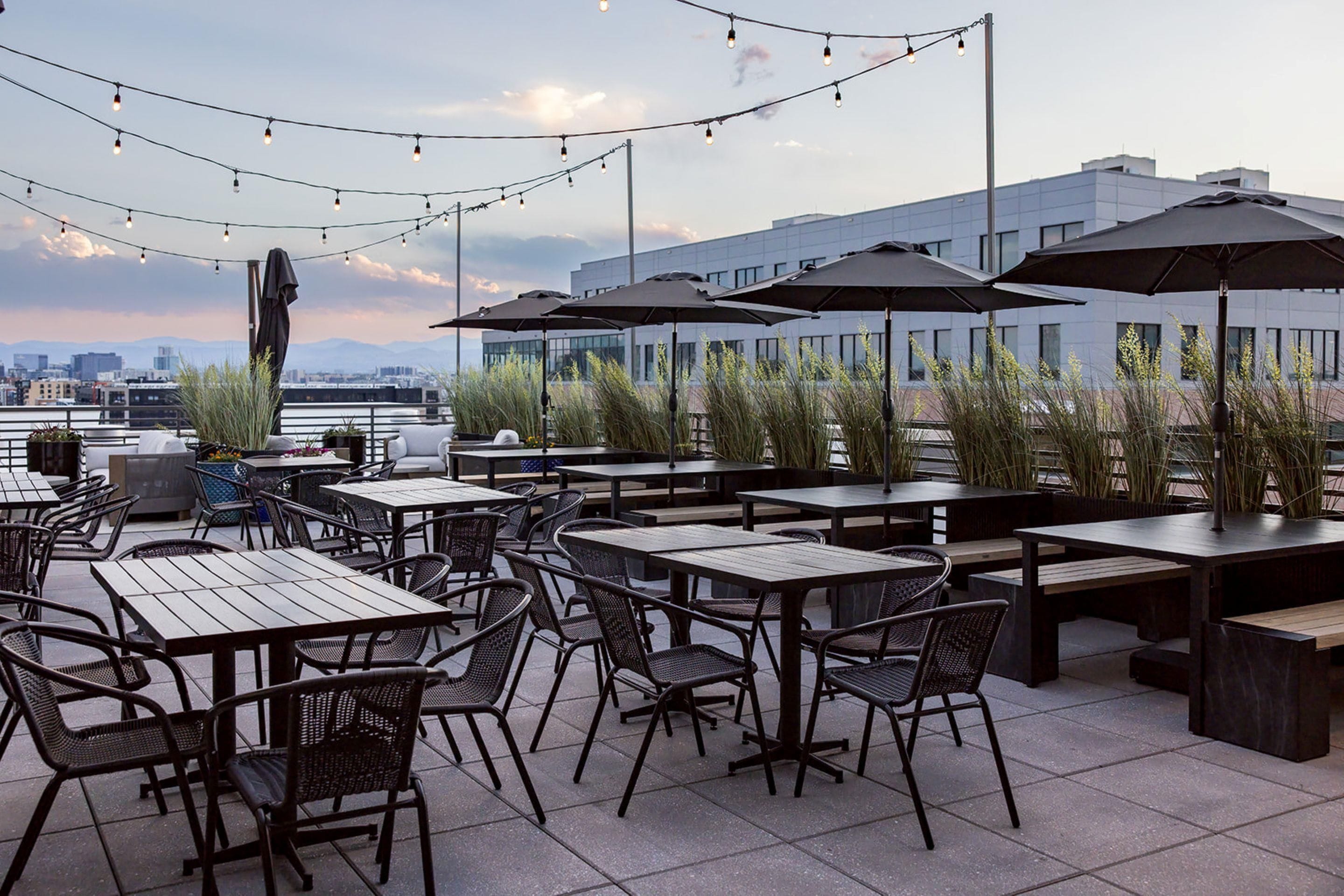 Un espace extérieur aménagé avec des tables, des chaises, des guirlandes lumineuses et des parasols.