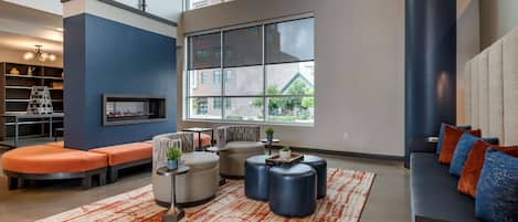 A modern living room with a sectional sofa, ottomans, a coffee table, and a large window offering a view of buildings and greenery.
