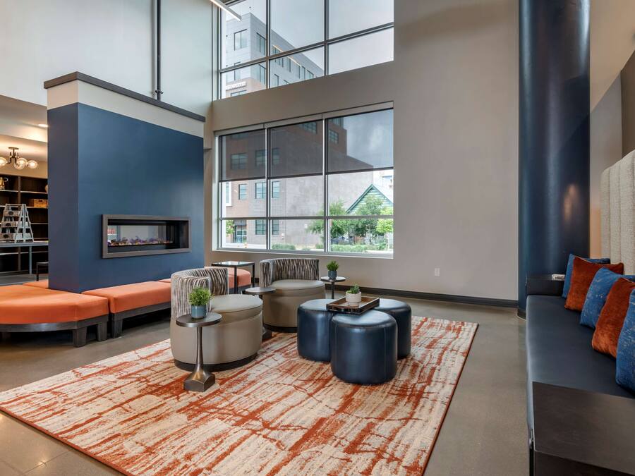 A modern living room with a sectional sofa, ottomans, a coffee table, and a large window offering a view of buildings and greenery.