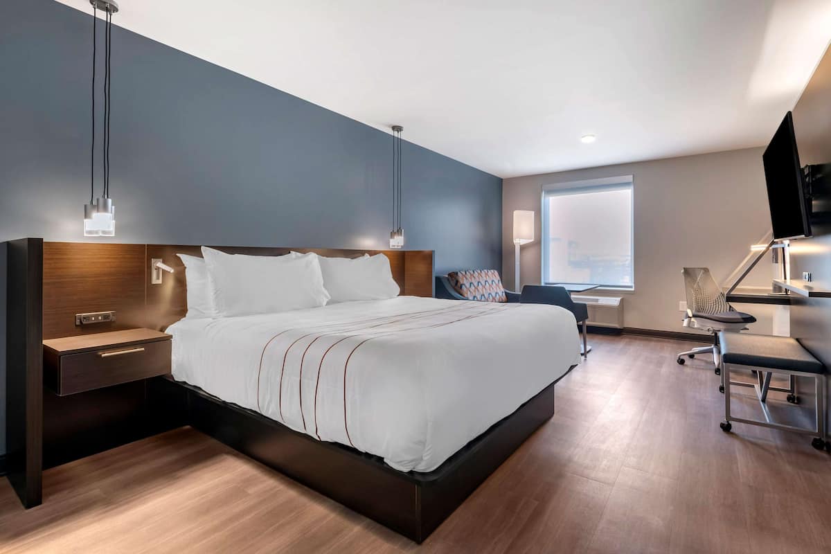 A modern hotel room with a large bed, bedside tables, a desk, and a TV.