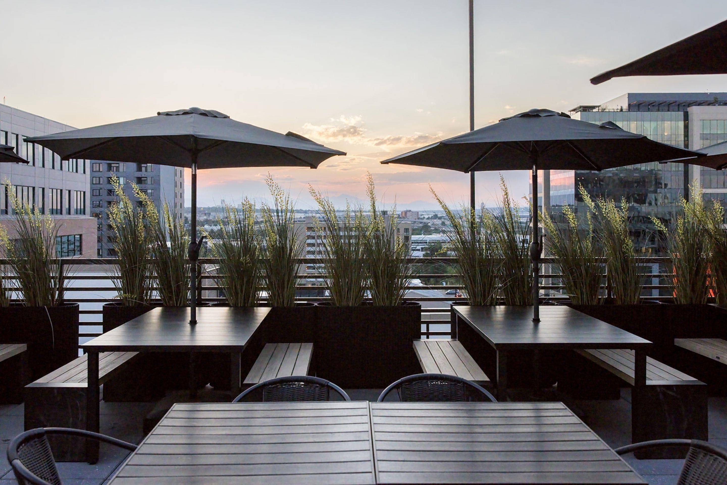 An outdoor seating area with tables and umbrellas, overlooking a cityscape.