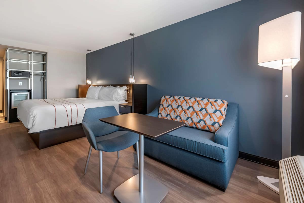 A modern hotel room with a bed, a sofa, a table, and a lamp.