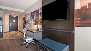 A modern hotel room with a flat-screen TV, a desk, a chair, and a bench.