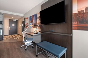 A modern hotel room with a flat-screen TV, a desk, a chair, and a bench.