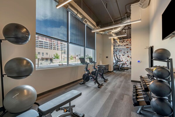 Ein Fitnessstudio mit Trainingsgeräten, großen Fenstern und Blick auf umliegende Gebäude.