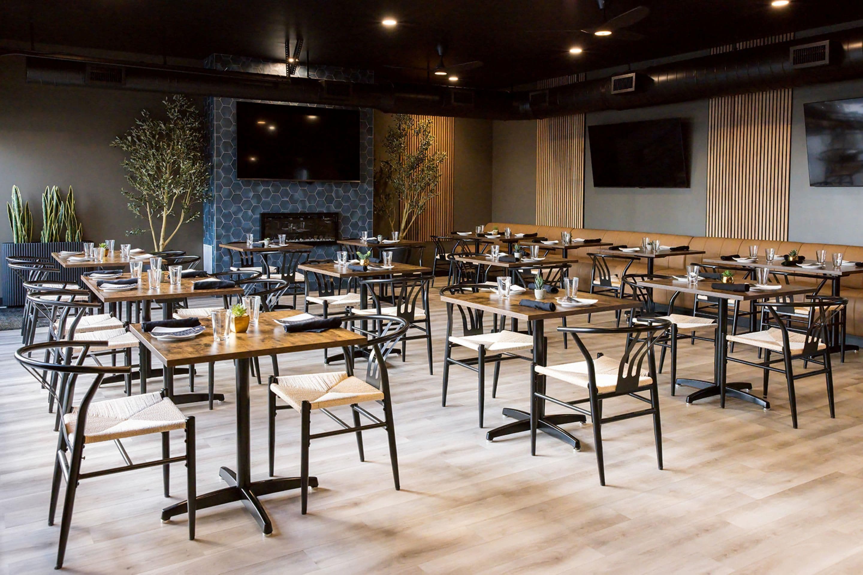 Un restaurante moderno con varias mesas y sillas, una chimenea y amplios ventanales.